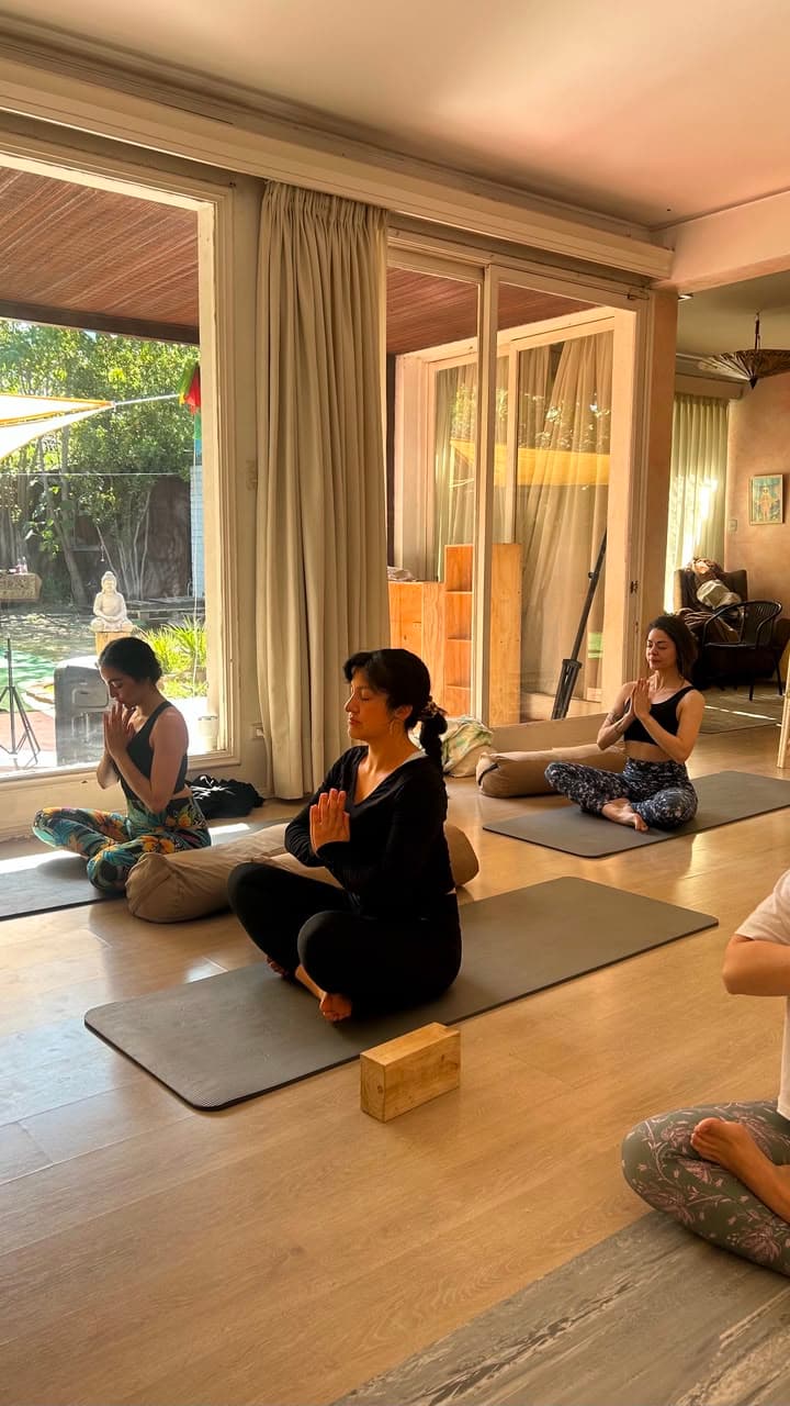 Alumnas meditando con las manos en oración, junto a un ventanal con vista al jardín